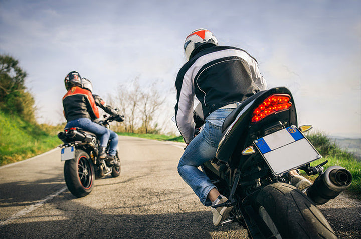 Two motorcycles, one with a passenger, shot from behind as they lean rounding a corner