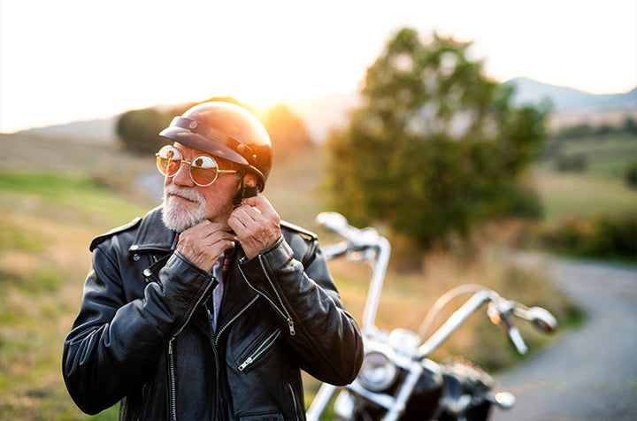 Older motorcycle rider strapping on helmet while riding in the country